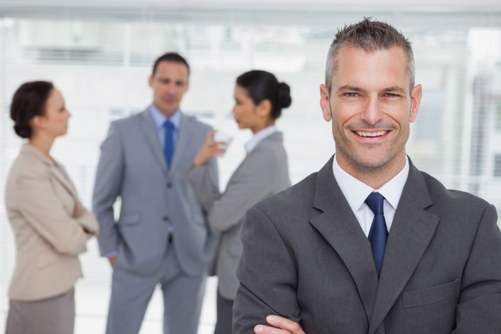 Smiling manager posing with employees in background in bright office